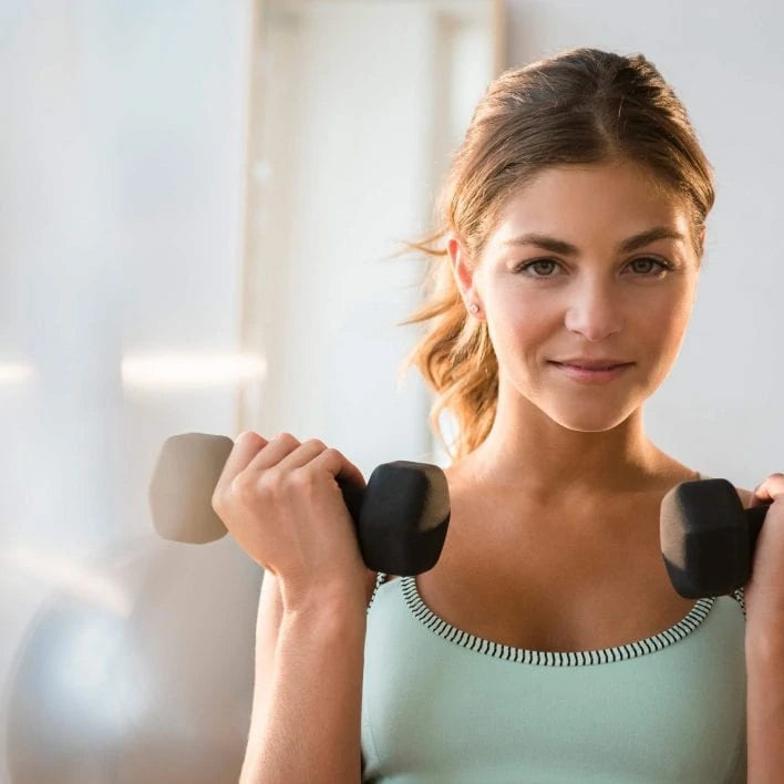 Junge Frau hat zwei Hanteln in der Hand und macht Sport