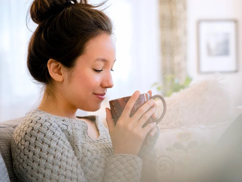 Eine Frau trinkt aus einer Tasse und sitzt auf einer Couch