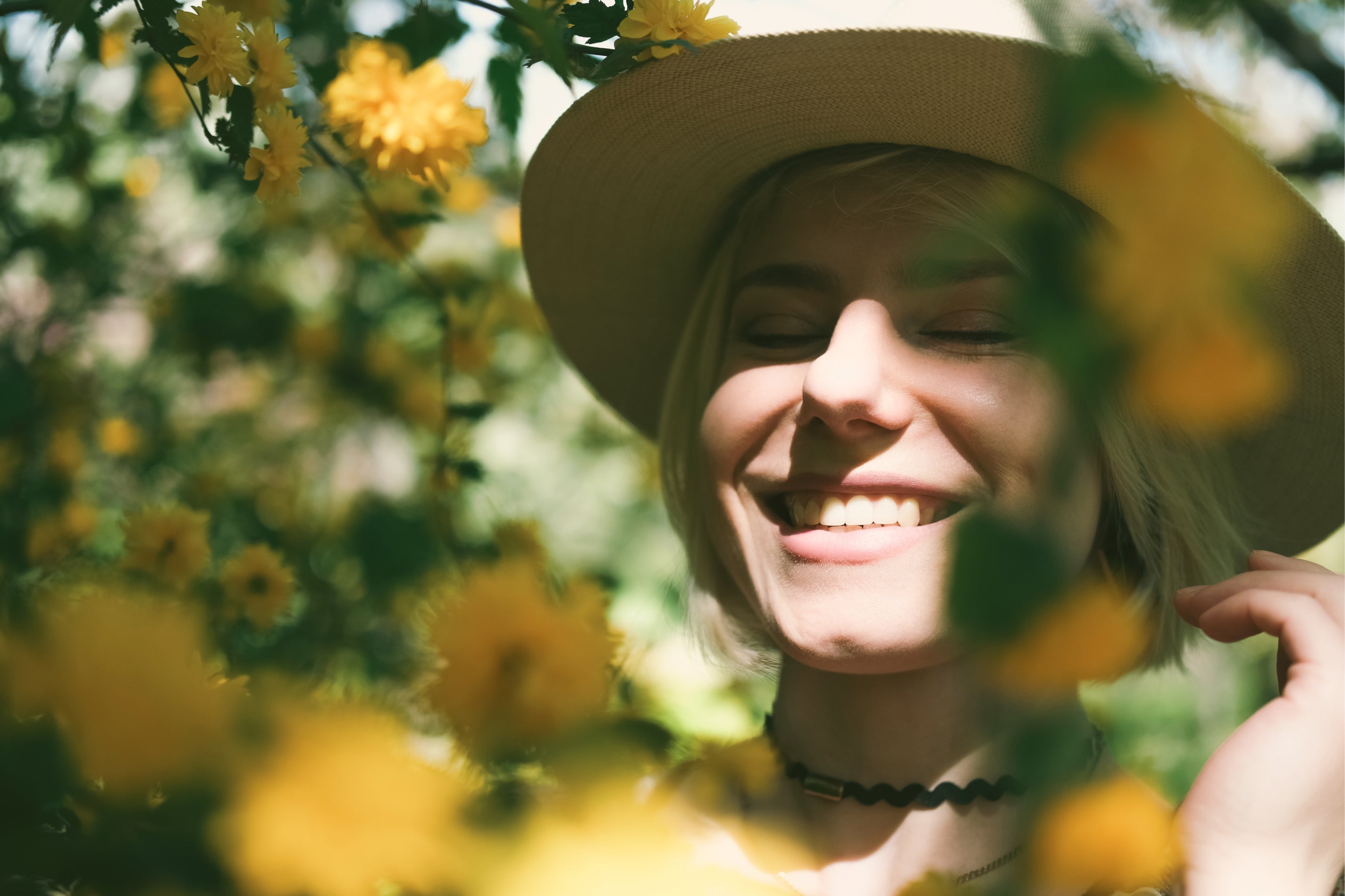 Eine Frau mit einem Sonnenhut steht hinter Blumen und grinst