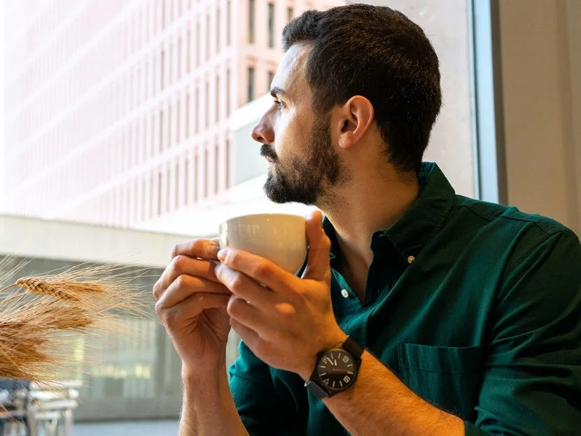 Mann hält eine Kaffeetasse in den Händen und sieht aus dem Fenster.